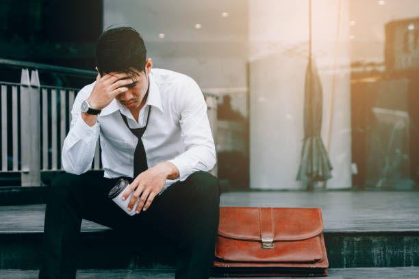 Asian young businessman stress sitting in front office with his hands covering his head against.