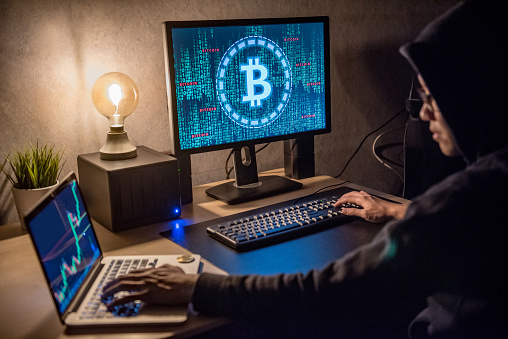 Hacker man using laptop and computer with Bitcoin green binary graphic and cryptocurrency candlestick graph price on monitor screen. Cyber crime digital currency laundering concept