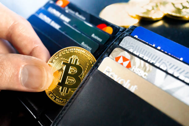 Bitcoin being taken out of a black leather wallet containing credit cards with bitcoins in the background. Photo taken in the UK in November 2022.